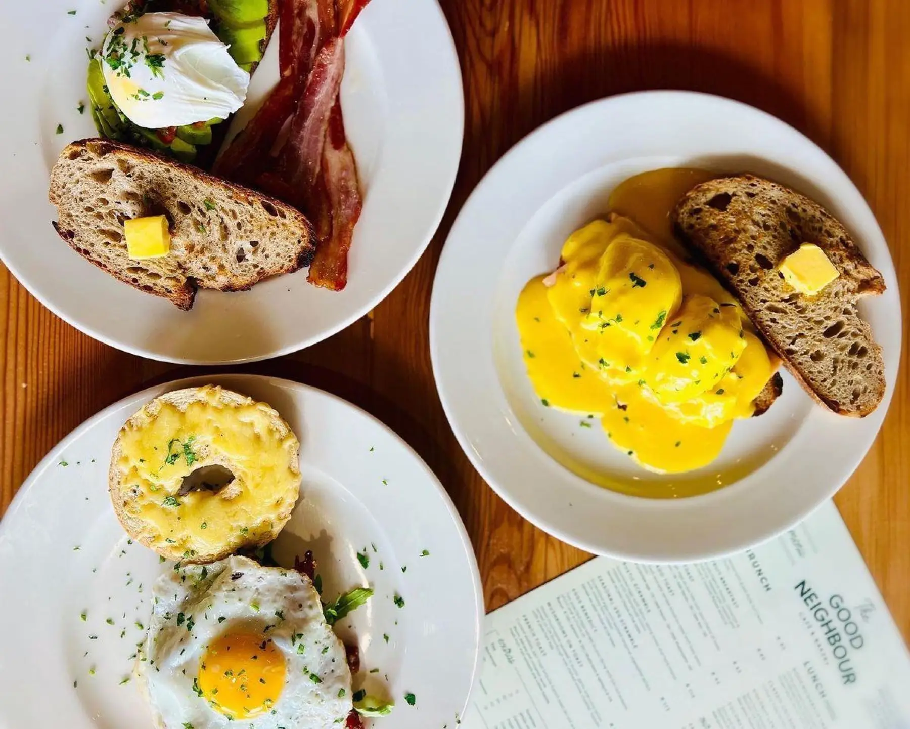 Three breakfast plates at The Good Neighbour — eggs benedict, avocado toast and a bagel